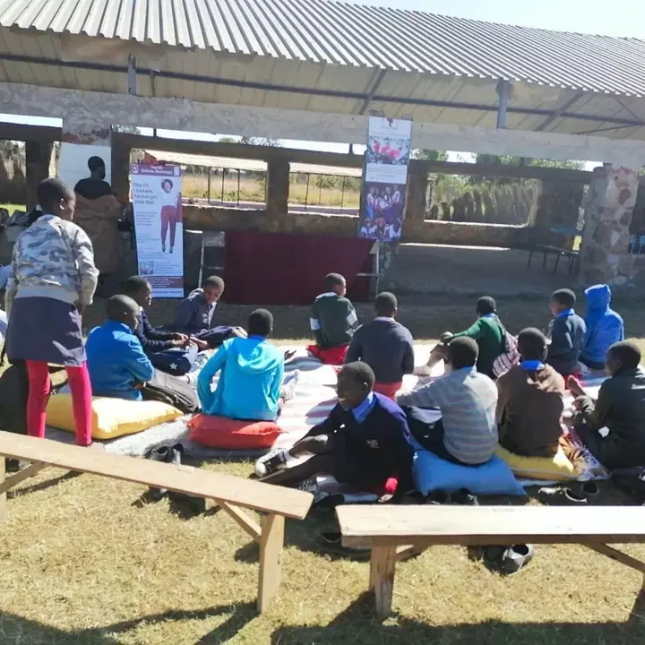 Children gathered outdoors on cushions during an earlier programme